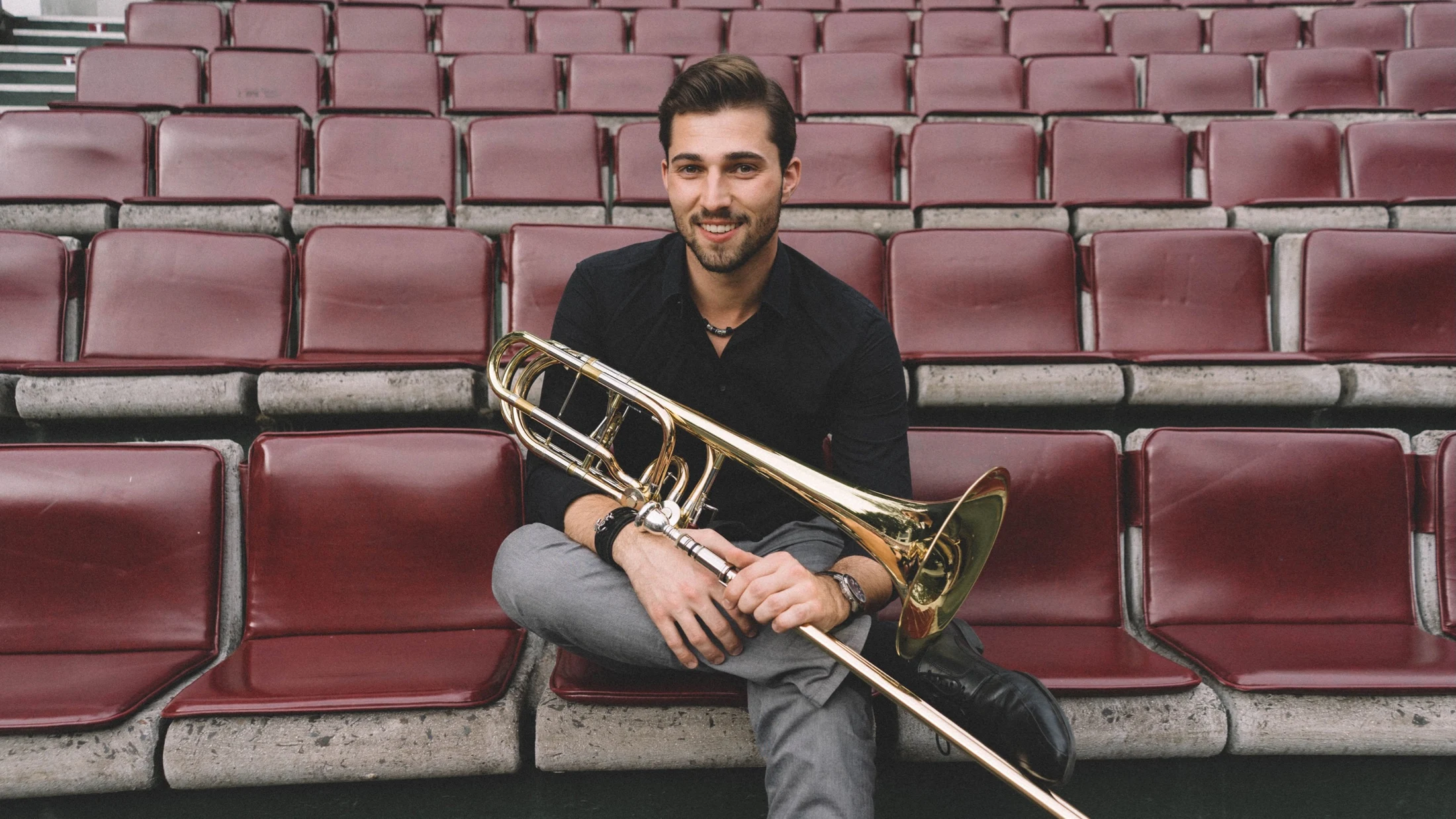 Andreas Kapellner sitzt mit Bassposaune zwischen roten Konzertsesseln
